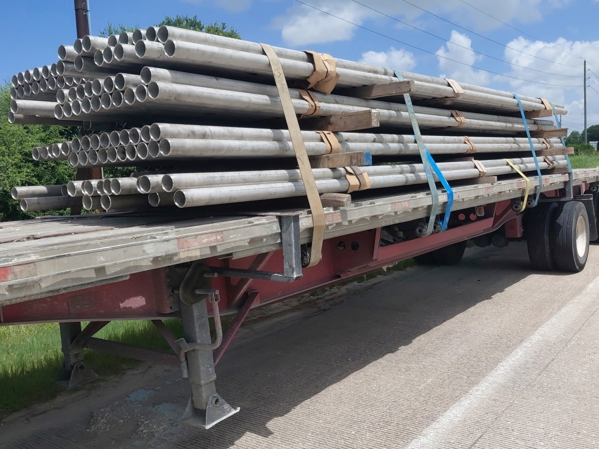 Flatbed trailer loaded with bundled steel pipe on a roadside shoulder