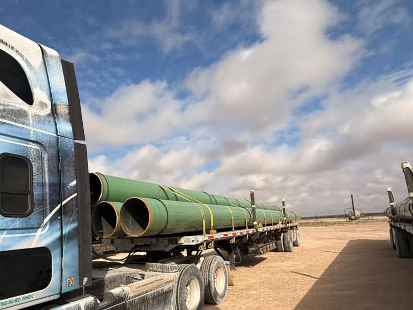 Flatbed trailer of green coated line pipe seen from behind the tractor on a West Texas pad