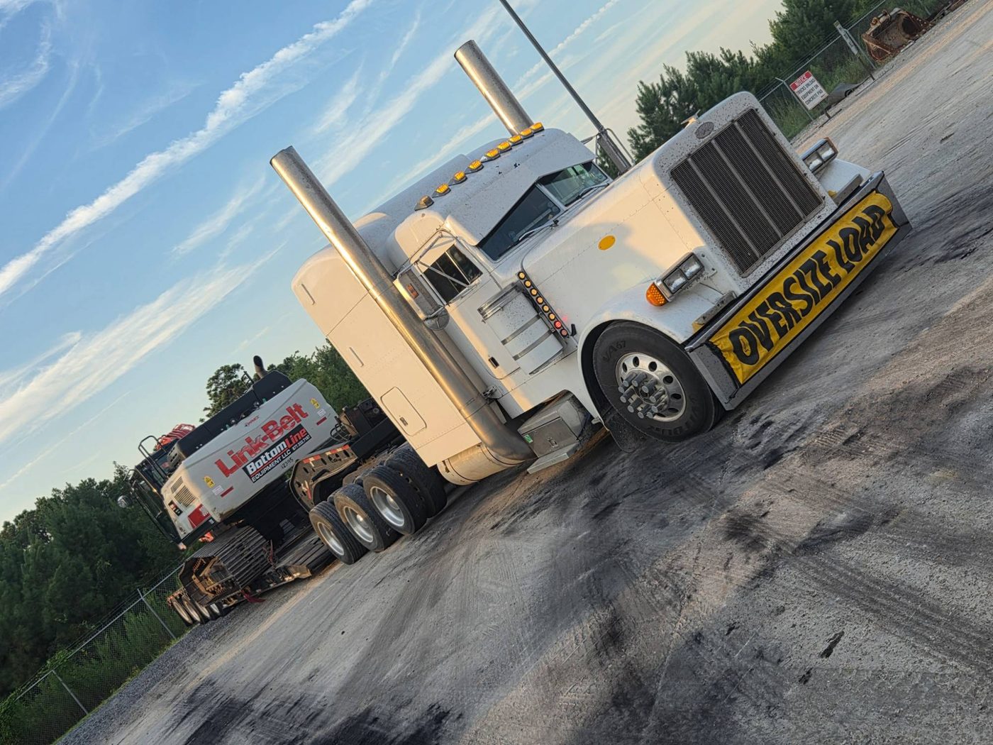 Peterbilt with an oversize load banner pulling a lowboy loaded with a crawler crane at a yard