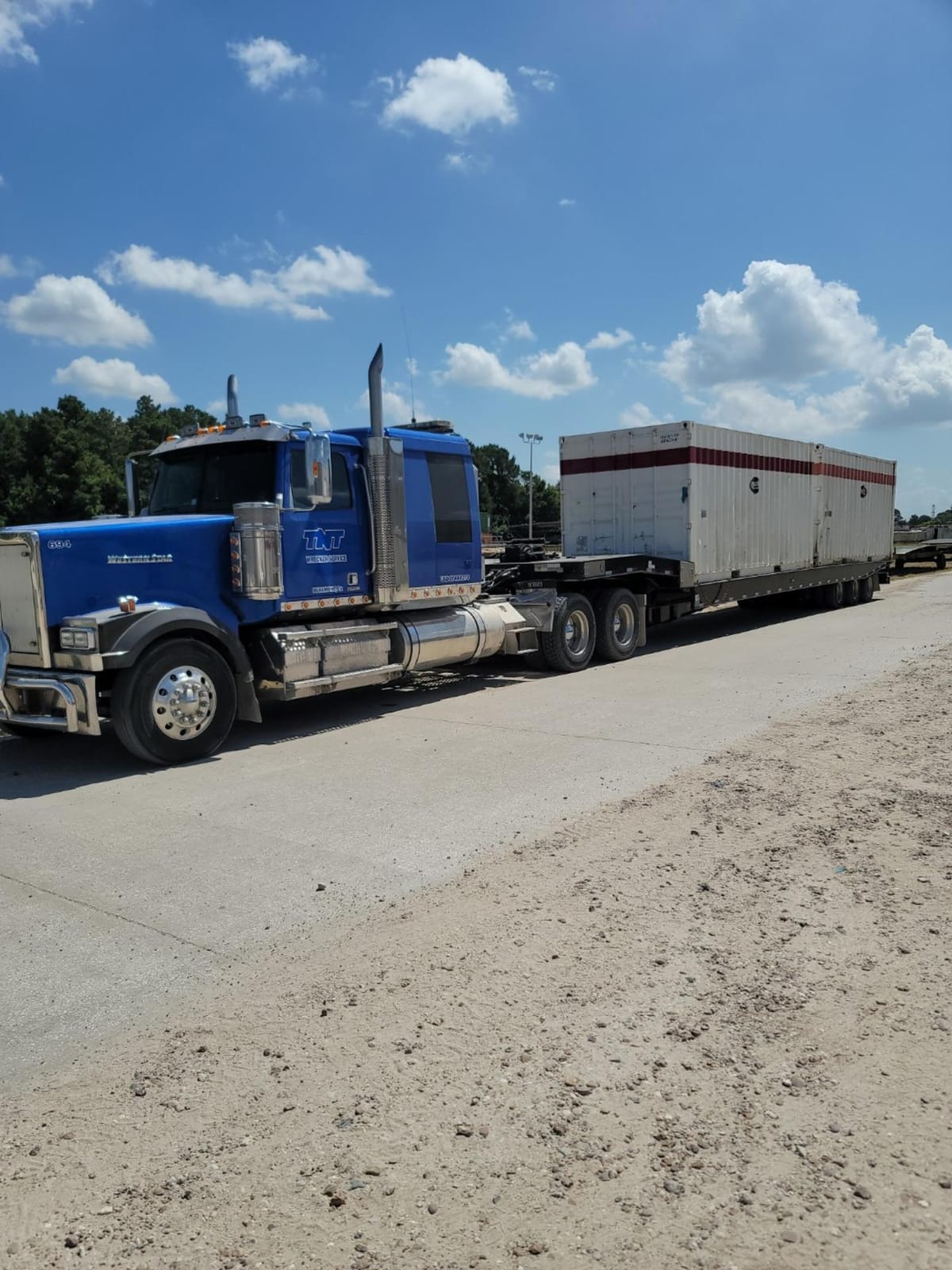 Blue semi truck hauling a flatbed trailer with a white container